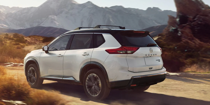 White Nissan Rogue SUV driving through a mountain landscape.